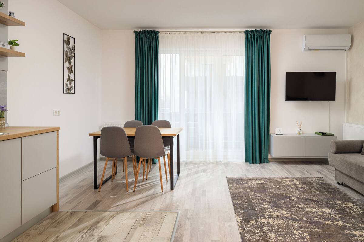 A modern living room with a dining area, a flat-screen TV, and a large window with curtains.