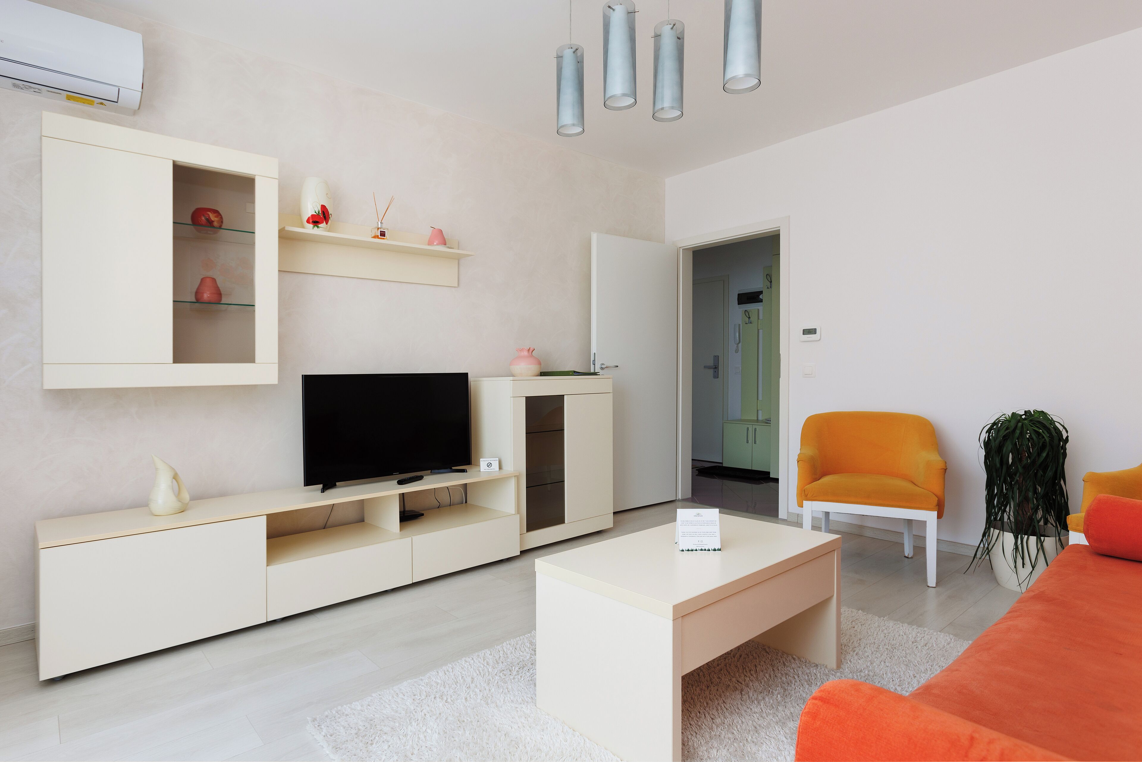Un salon moderne avec un téléviseur, des meubles blancs et un fauteuil orange vif.