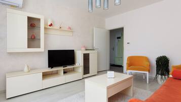 Un salon moderne avec un téléviseur, des meubles blancs et un fauteuil orange vif.