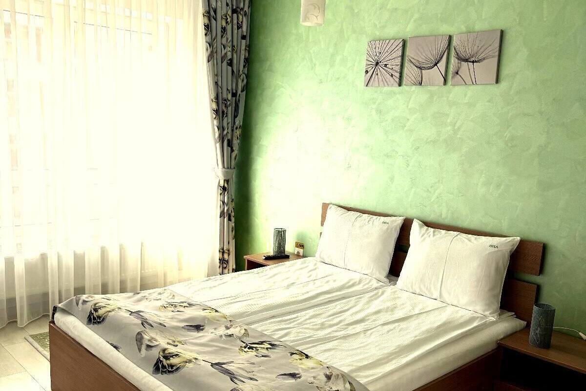 A bedroom with a wooden bed, green walls, and a window with sheer curtains.