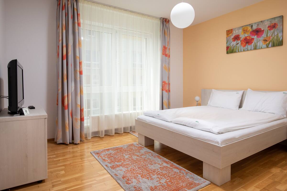 A bedroom with a bed, a desk, a television, and a painting on the wall.