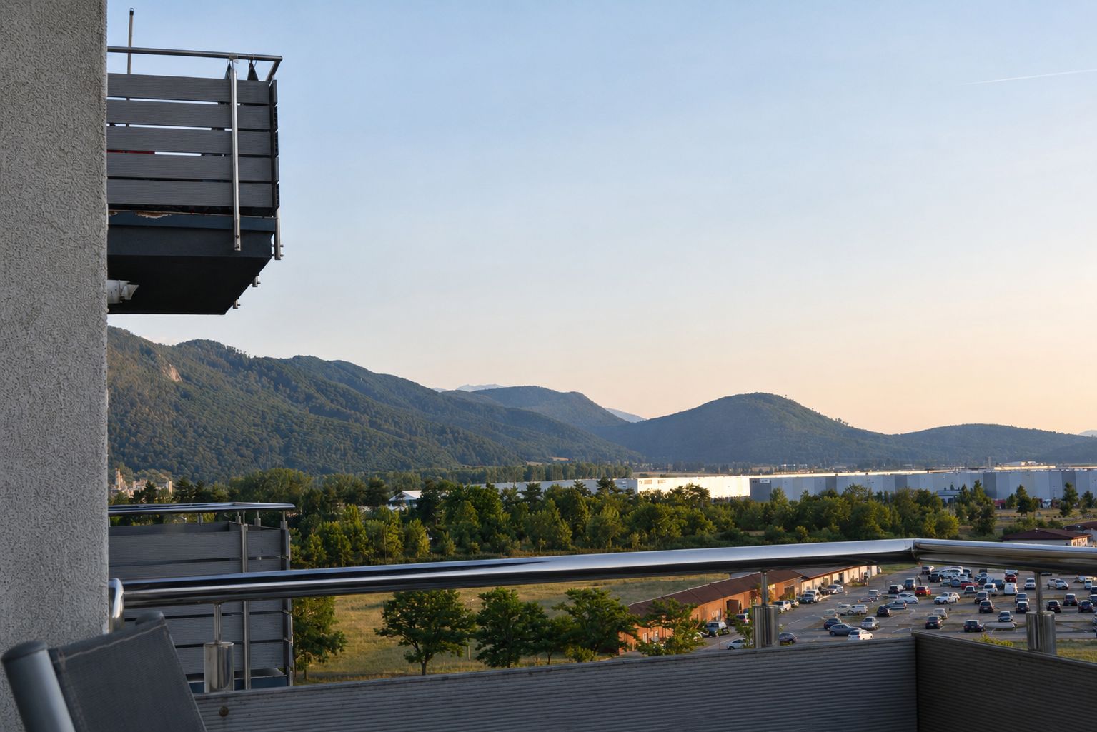 A balcony with a view of a parking lot, mountains, and a body of water.