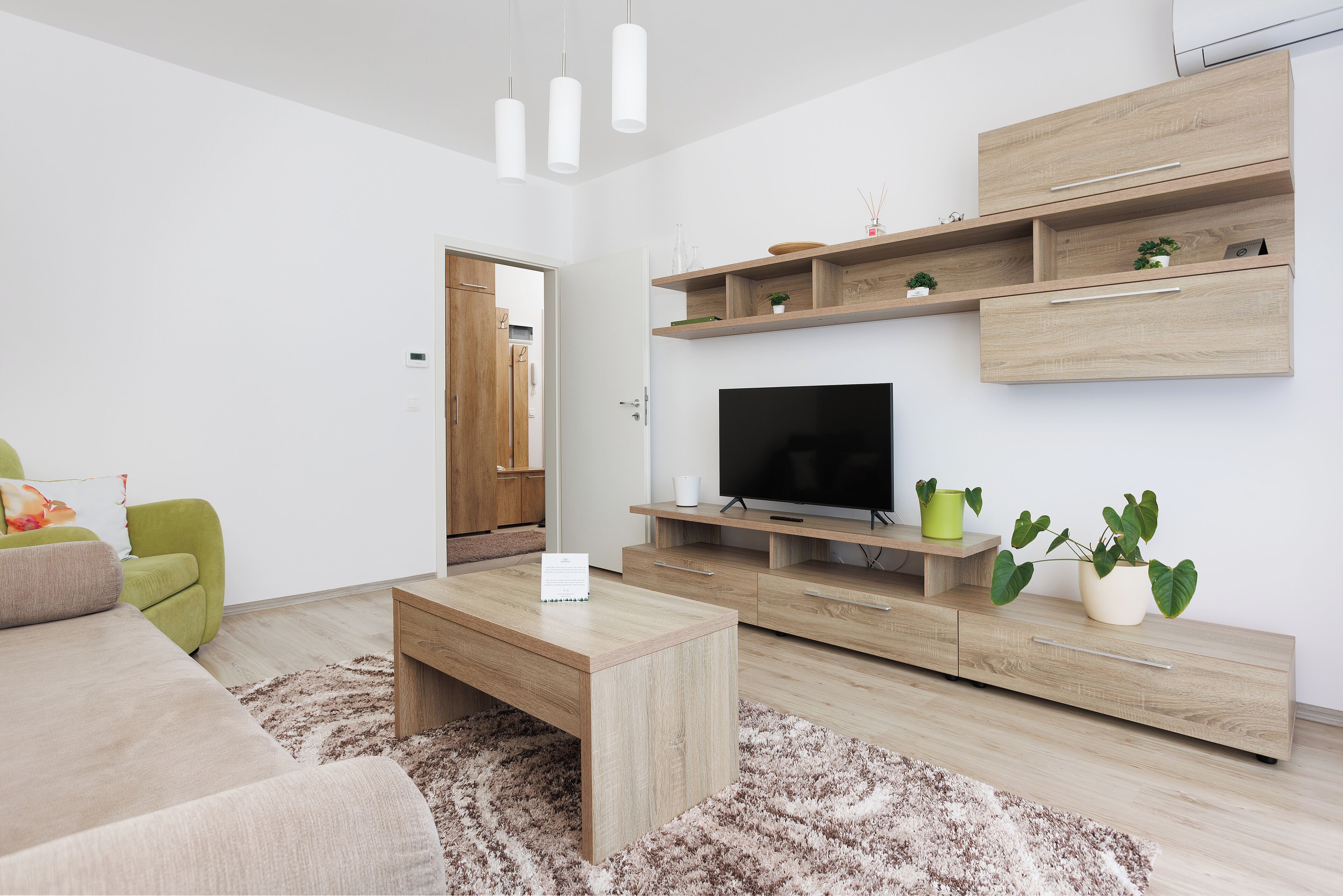 A modern living room with a flat-screen TV, wooden furniture, and a green chair.