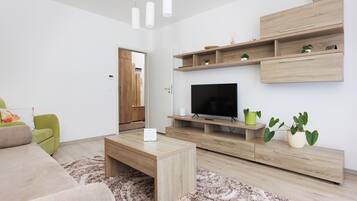 A modern living room with a flat-screen TV, wooden furniture, and a green chair.