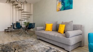 A modern living room with a grey sofa, yellow cushions, a blue chair, a glass coffee table, and a spiral staircase. - Brasov Holiday Apartments (Brasov)