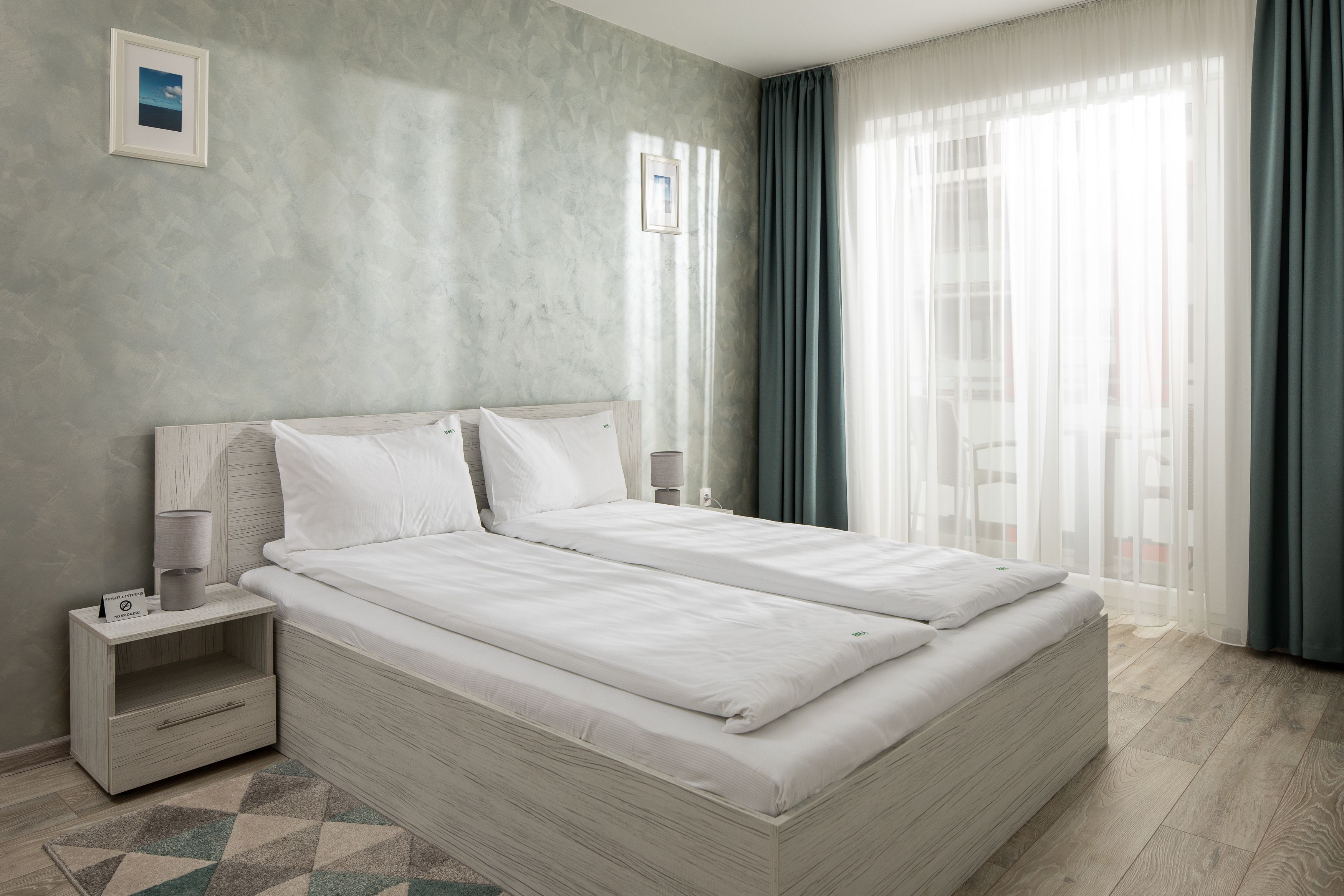 A modern bedroom with a large bed, bedside tables, and a view of the outdoors through sheer curtains.