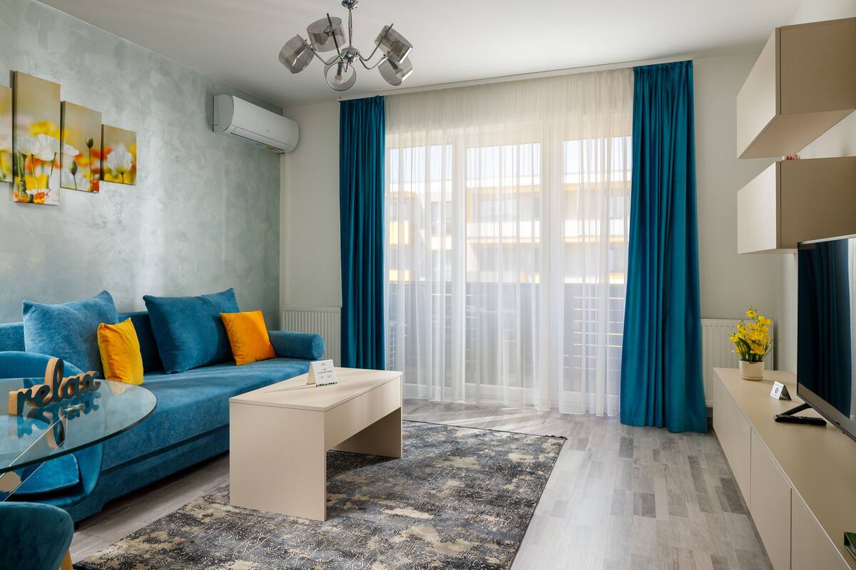 A modern living room with a blue sofa, a glass coffee table, and a TV on a cabinet.