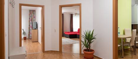 A spacious living area with a wooden floor, a dining table with chairs, a red sofa, and a potted plant.