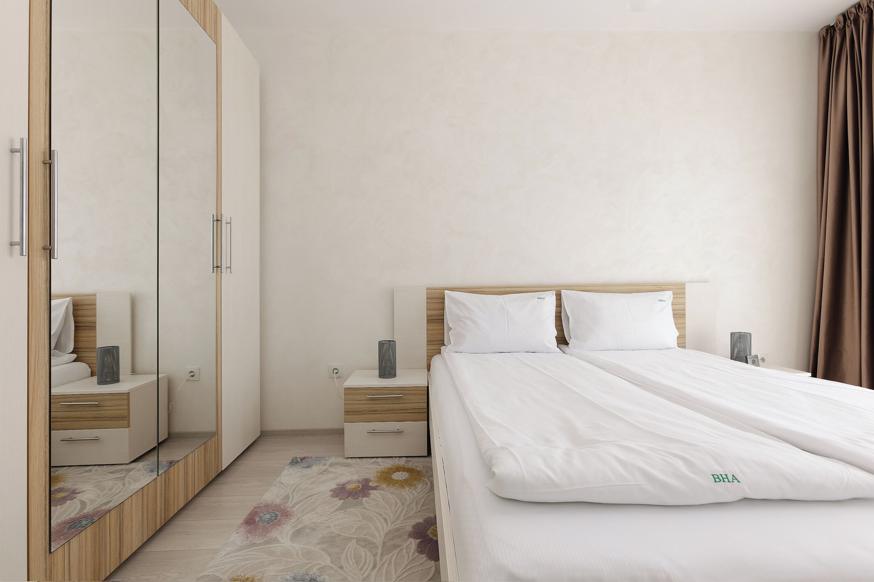 Un dormitorio ordenado con cama, mesitas de noche, un armario y un espejo.