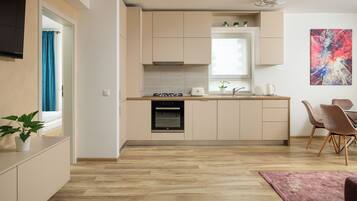 A modern kitchen with light wood flooring, a built-in oven, and a dining area with a table and chairs.