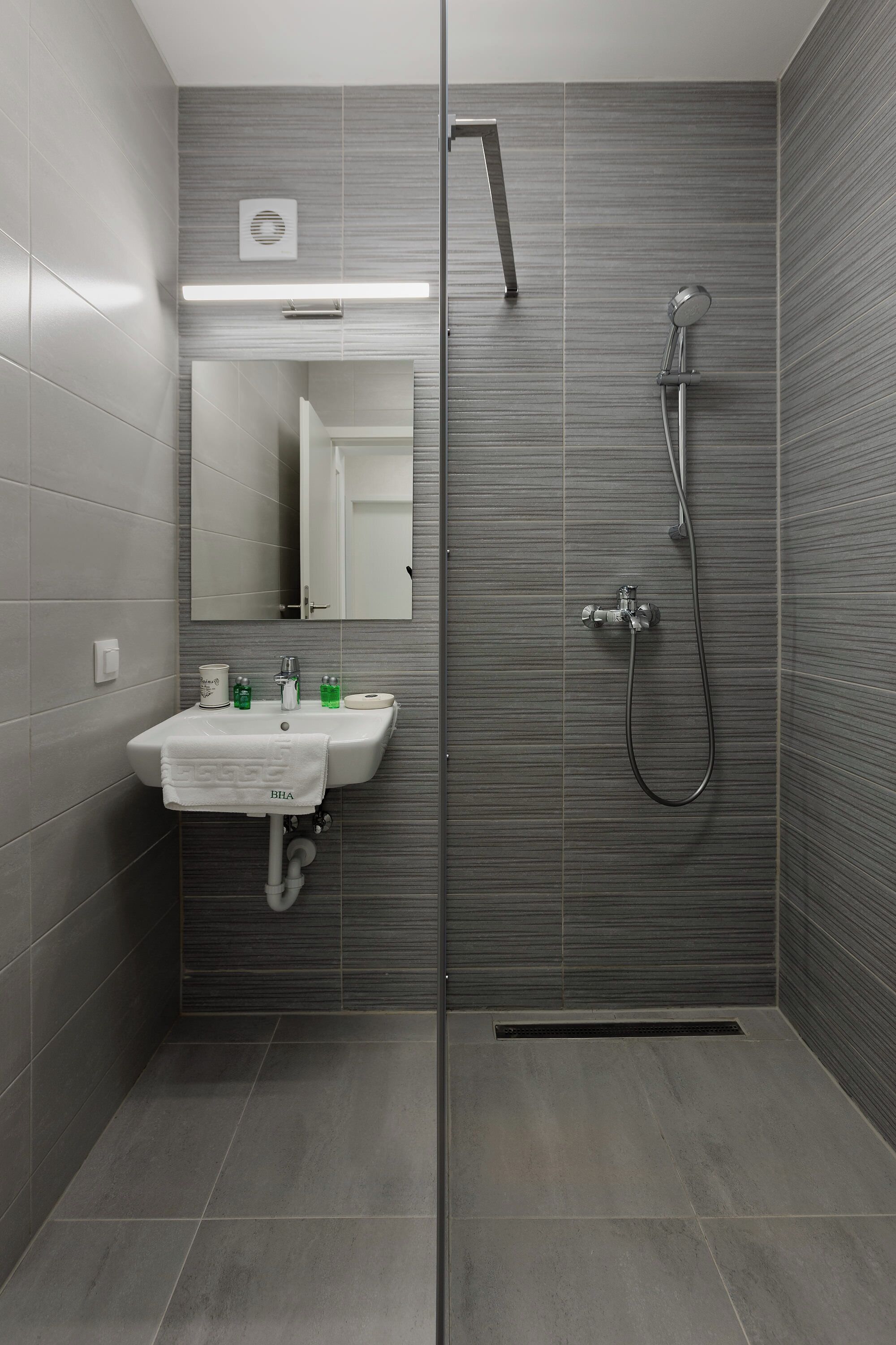 Un baño moderno con ducha envuelta en vidrio, un lavabo con toalla y un espejo encima.