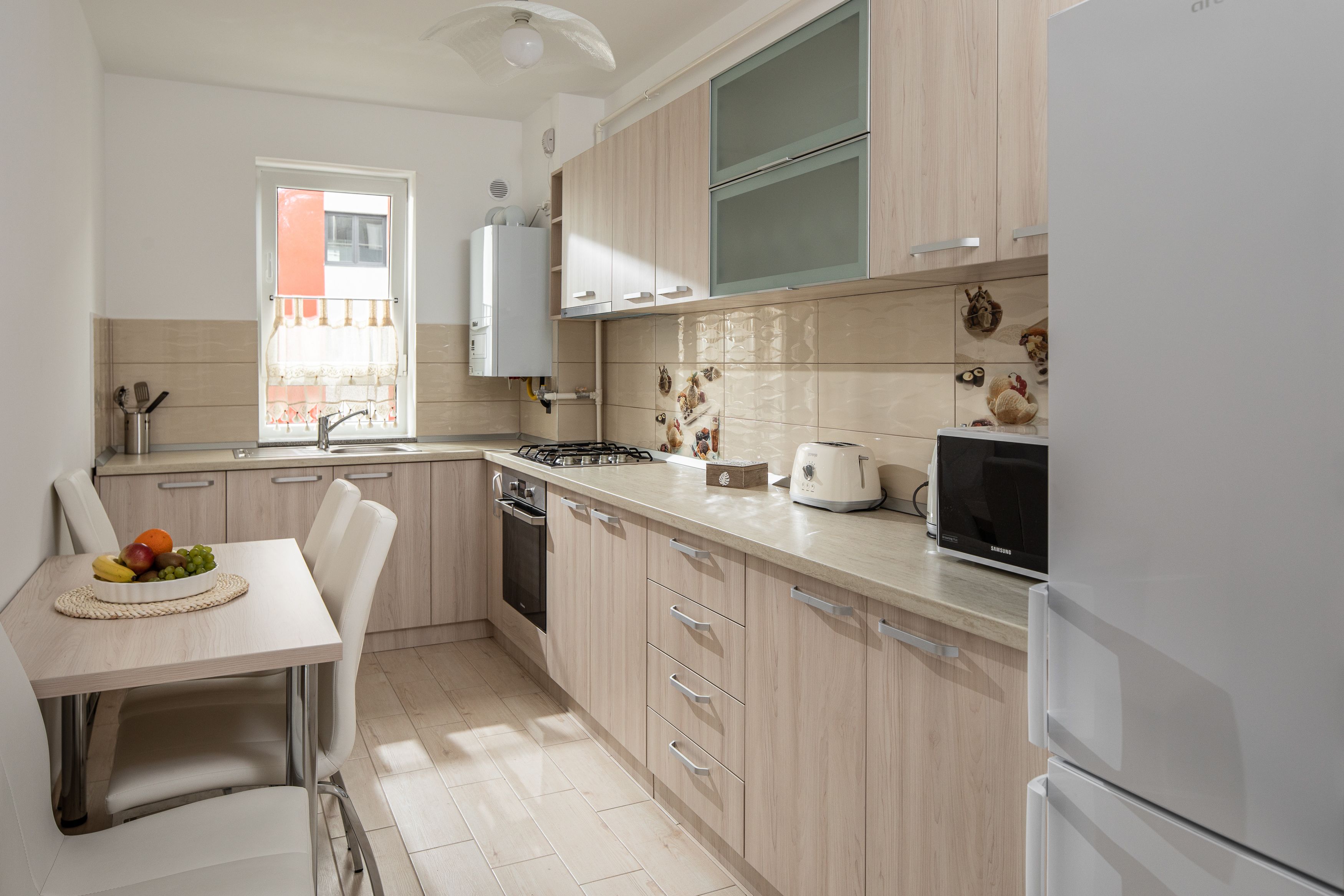A modern kitchen with light wood cabinets, a stainless steel sink, a gas stove, and a built-in microwave.