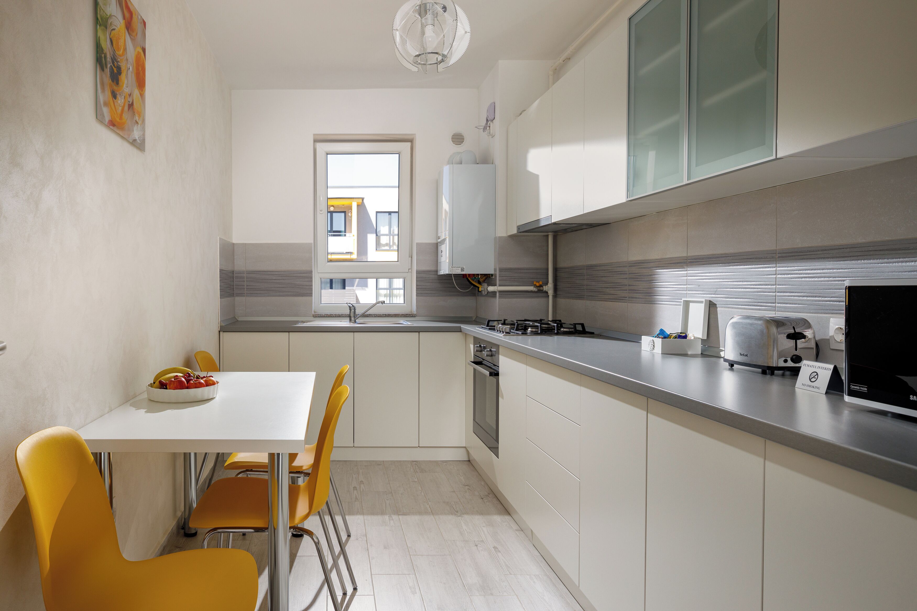 A modern kitchen with a white table, yellow chairs, a window, and a built-in oven.