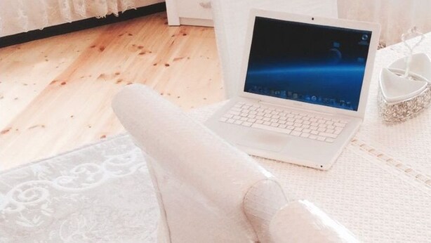 Ein weißer Laptop auf einem strukturierten weißen Teppich, ein weißer Stuhl und ein kleines, weißes Deko-Objekt auf einem Tisch.