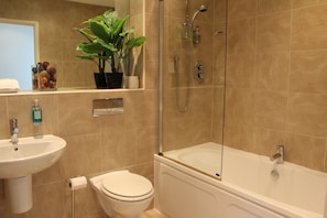 Un baño con lavamanos, inodoro y bañera. Hay una planta en maceta sobre el lavabo.
