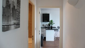 A hallway leading to a kitchen with a black and white cityscape photo on the wall, a potted plant, and a folding chair.