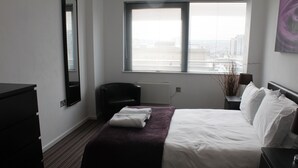 A hotel room with a bed, a chair, a dresser, and a window with blinds.