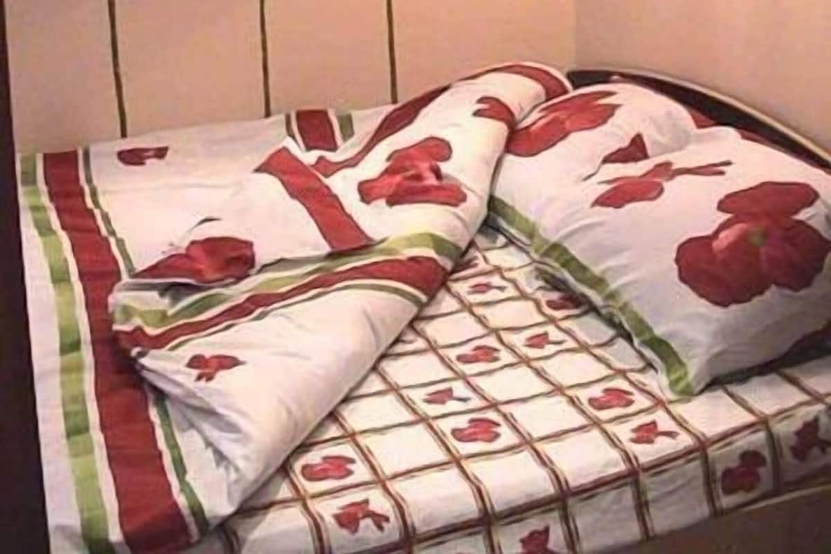 A bed with a floral-patterned bedspread and pillows, a wall-mounted lamp, and a wall with a floral design.
