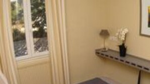 A room with a bed, a window, a small table with a lamp, and a framed picture on the wall. - Hôtel les Terrasses du Rove (Le Rove)