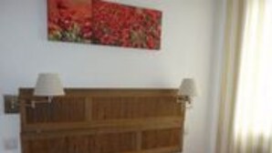 A bedroom with a wooden headboard, two bedside lamps, a bed with colorful pillows, and a painting on the wall. - Hôtel les Terrasses du Rove (Le Rove)