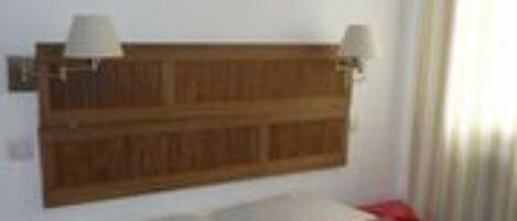 Une chambre à coucher avec une tête de lit en bois, deux lampes de chevet, un lit agrémenté d’oreillers colorés et un tableau accroché au mur.