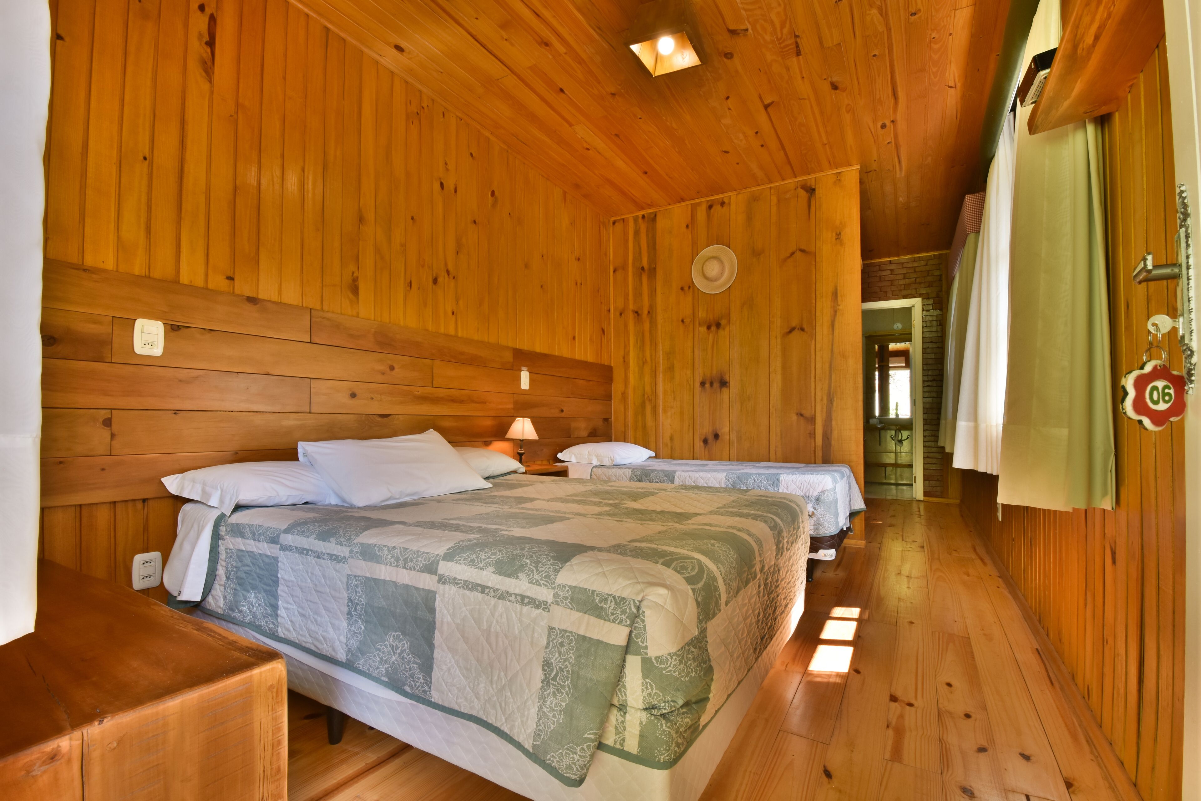 A wooden cabin room with two beds, a nightstand, and a lamp.
