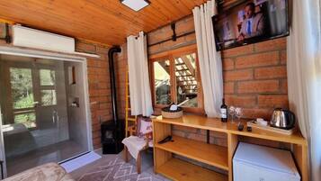 Una habitación acogedora con techo de madera, un televisor en la pared, una mesa pequeña con una cesta, una silla y un refrigerador.