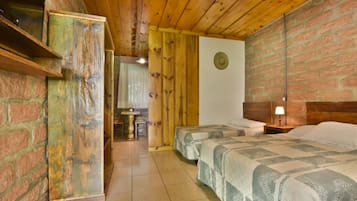 Ein Zimmer mit zwei Betten, Holzwänden, einer Ziegelwand, einer Holzbalkendecke, einem kleinen Tisch mit Lampe und einer Tür.