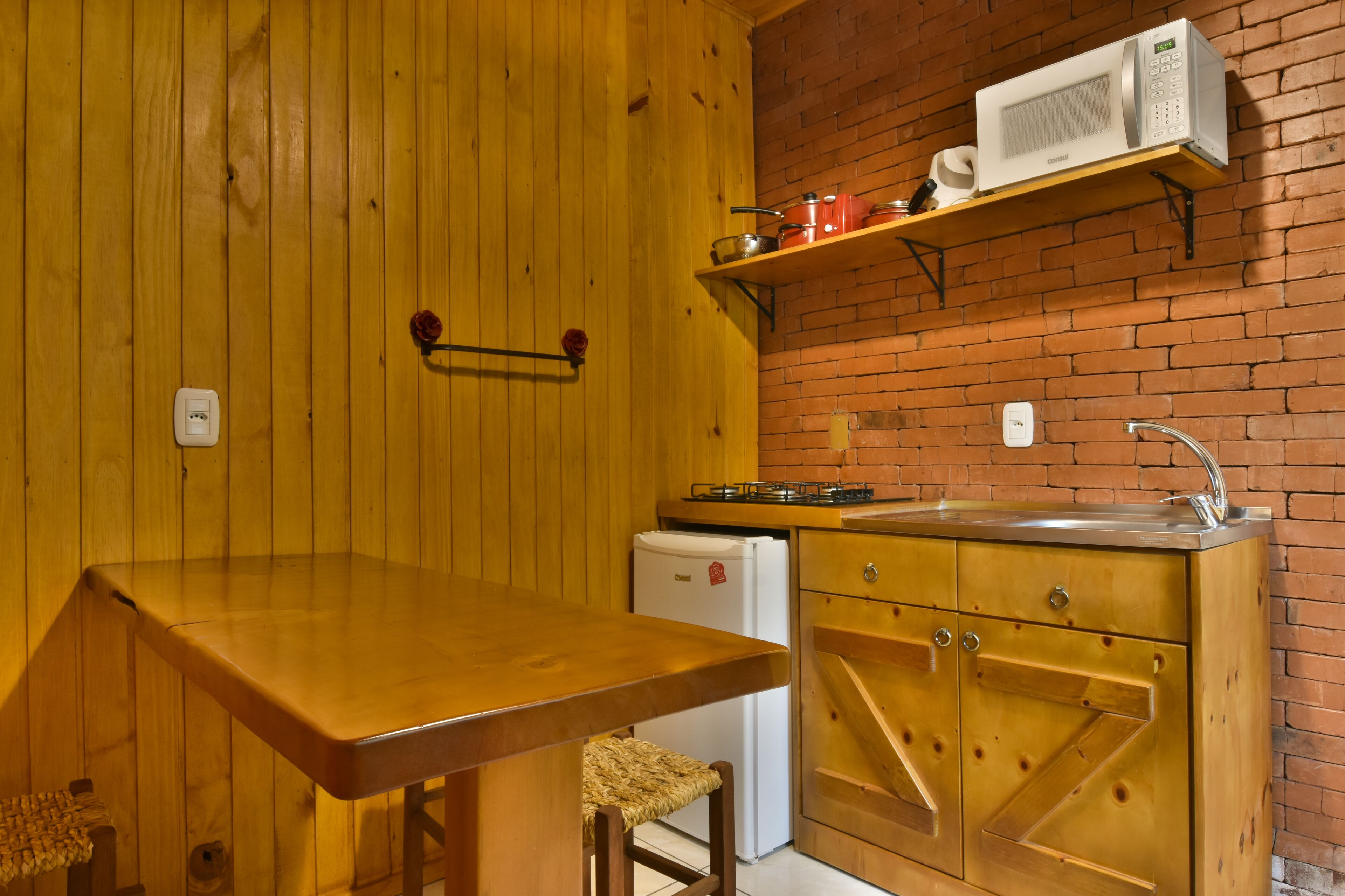Una cocina compacta con paredes de madera, un estante con microondas integrado, un refrigerador pequeño y una mesa de madera.