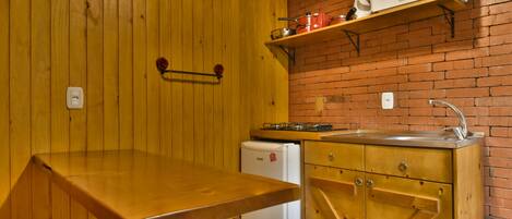 Una cocina compacta con paredes de madera, un estante con microondas integrado, un refrigerador pequeño y una mesa de madera.