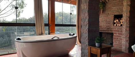 Una habitación amplia con una bañera grande, una chimenea de ladrillo y vistas a través de amplios ventanales.