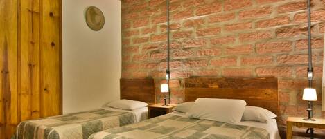 Una habitación con dos camas, paredes de madera y un muro de ladrillo.