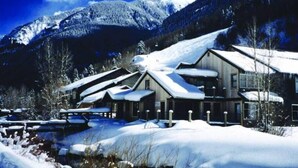 Eine schneebedeckte Lodge mit mehreren Hütten, umgeben von Bergen und einem klaren Himmel.