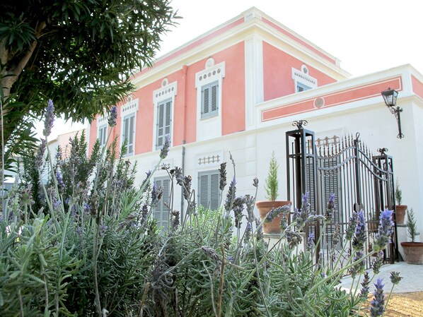 A building with a pink facade, white trim, and a gated entrance. - Antica Dimora la Porta del Sale (Marsala)