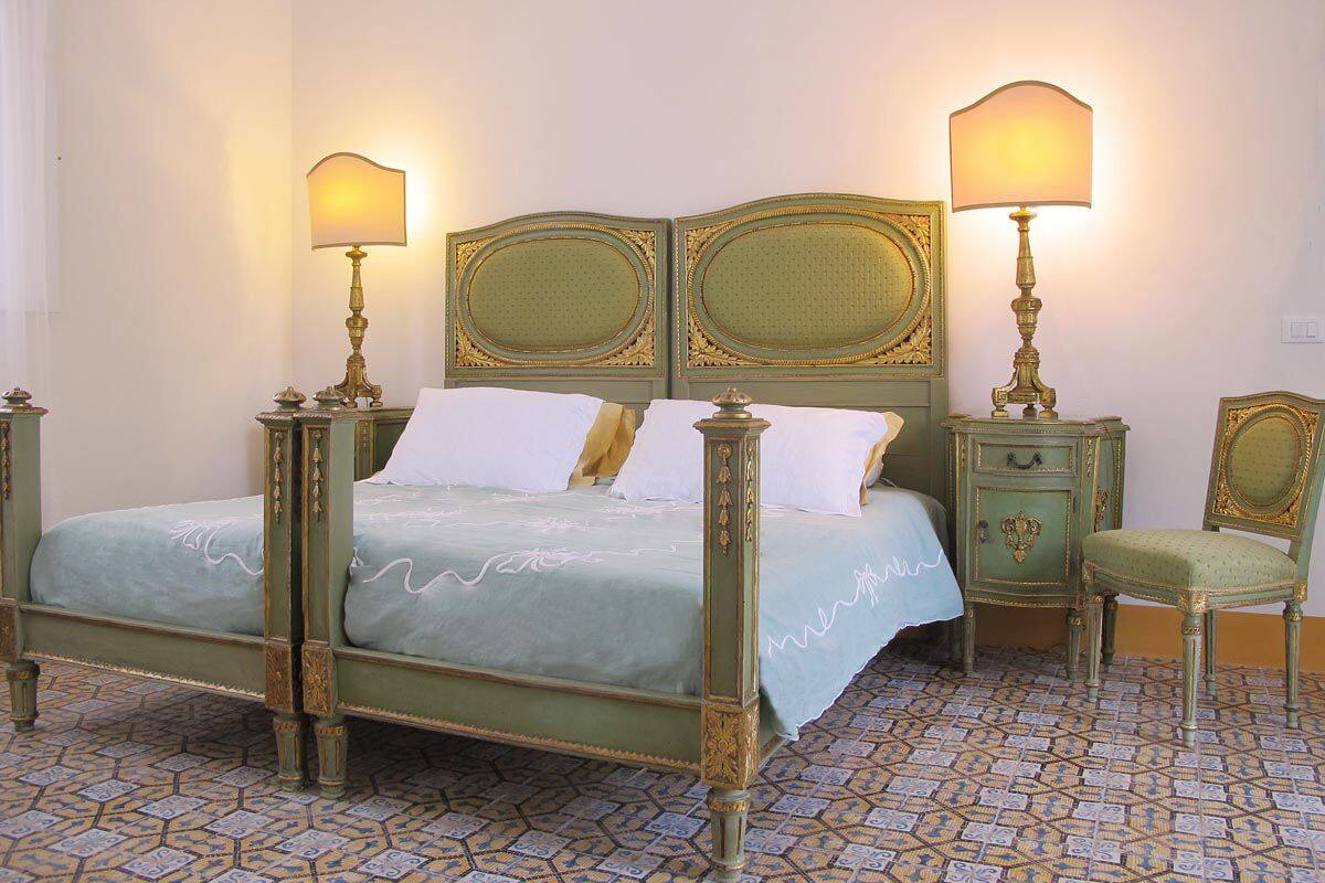 Un lit à baldaquin avec une tête de lit rembourrée de tissu vert, deux tables de chevet avec des lampes et une chaise assortie.