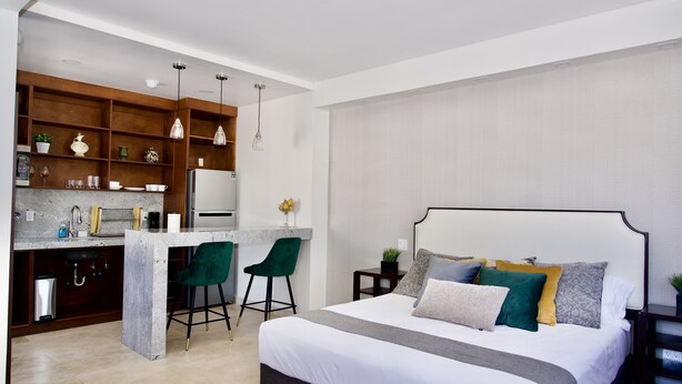 A modern bedroom with a large bed, a small kitchenette, and a dining area. - Rio Suites (Tijuana)