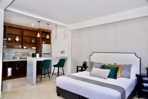 A modern bedroom with a large bed, a small kitchenette, and a dining area. - Rio Suites (Tijuana)