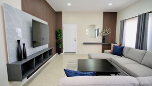 A modern living room with a grey sofa, a flat-screen TV mounted on a marble wall, a coffee table, and a potted plant. - Rio Suites (Tijuana)