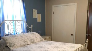Ein Schlafzimmer mit Bett, Deckenventilator, Tür und einem Fenster mit Vorhängen.