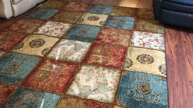 Ein Wohnzimmer mit einem beigen Sofa, einem blauen Sessel und einem farbenfrohen Patchworkteppich.