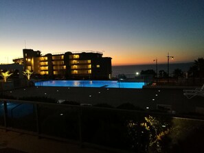 Un hôtel doté d’une piscine, de plusieurs balcons et offrant une vue sur la mer au crépuscule.