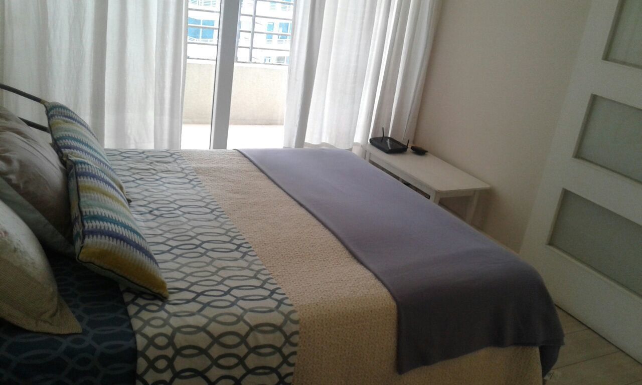 A bedroom with a bed, a bedside table, and a window with curtains.