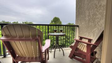 Un balcón con dos sillas Adirondack, una pequeña mesa redonda con dos copas de vino y vistas a un paisaje verde.