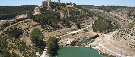 Un castillo en una colina con vista a una masa de agua, un puente y un pequeño edificio cerca del agua.