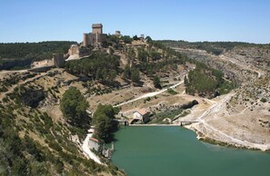 A castle on a hill overlooking a body of water with a bridge and a small building near the water. - Hotel Hierbaluisa (Alarcon)