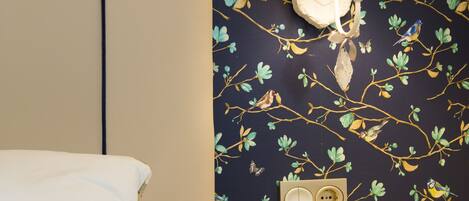 Un dormitorio con cama, una mesita de noche con lámpara y un papel tapiz floral en la pared.