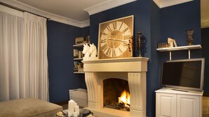 Una sala de estar con chimenea, un reloj grande y un televisor sobre un mueble.