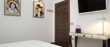 A hotel room with a bed, a desk with a lamp, and two paintings on the wall.