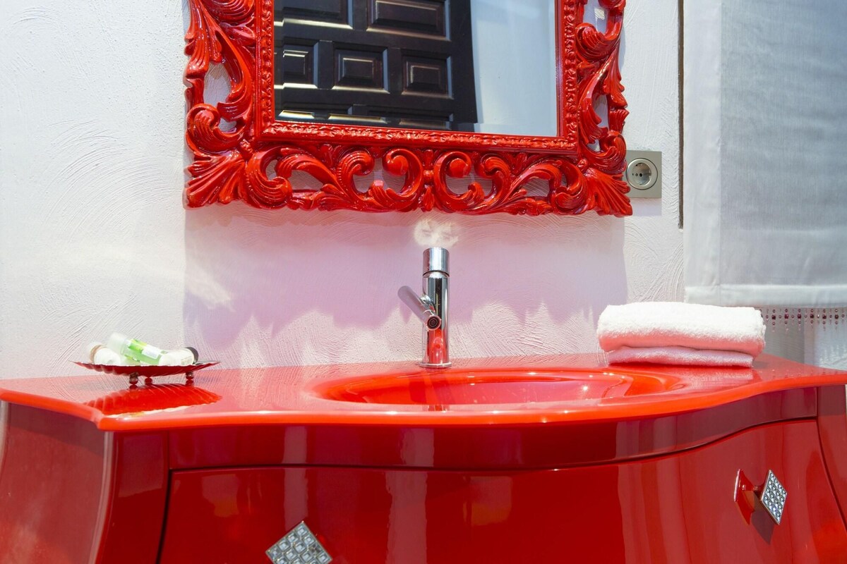 Un tocador de baño rojo con espejo, lavamanos y una toalla.