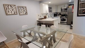A modern kitchen with stainless steel appliances, a glass dining table, and white cabinetry.